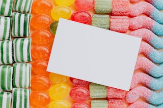 Closeup from above of white paper card composed on rows of delicious caramel gummy jelly sweets in modern candy shop