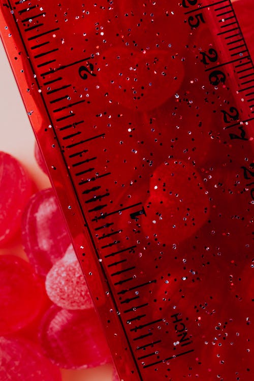 Closeup of assorted raspberry sour sweets and caramel candies placed together near red ruler with sparkles in contemporary candy shop