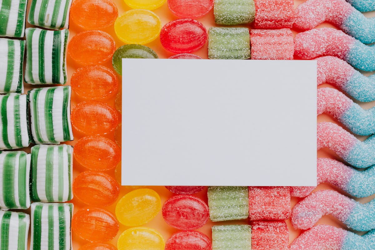 Top view closeup of blank paper card placed on multicolored various shapes yummy candies in light confectionery