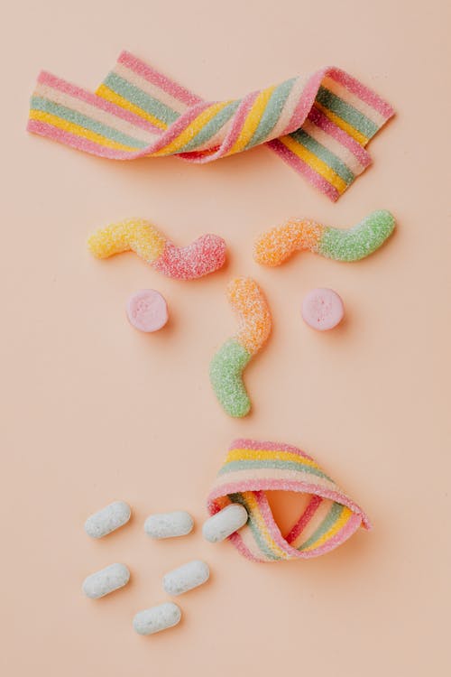 Free From above of various delicious gummy sweets and dragees arranged as coughing person with wrinkled eyebrows and curly hair in candy store Stock Photo