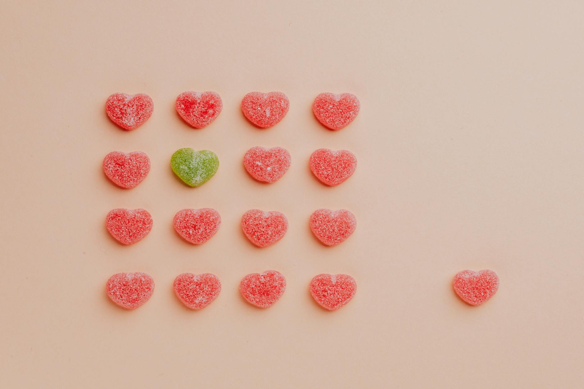 Top view of delicious sprinkled jelly sweets composed in lines with one candy aside on pink backdrop in candy shop