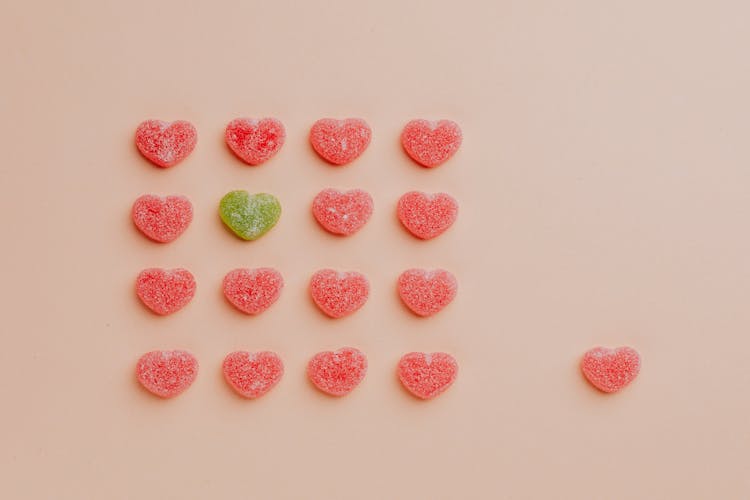 Heart Shaped Gummy Candy Assorted In Rows With One Candy Aside Against Pink Background