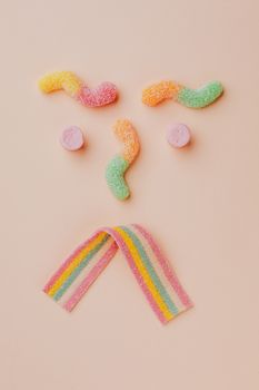 在米色的背景上，色彩缤纷的软糖被创造性地排列成一张脸