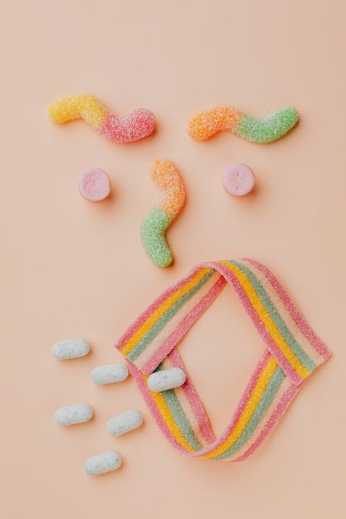 Top view of different gummy worms dragees and candies arranged together as yelling face in modern confectionery shop