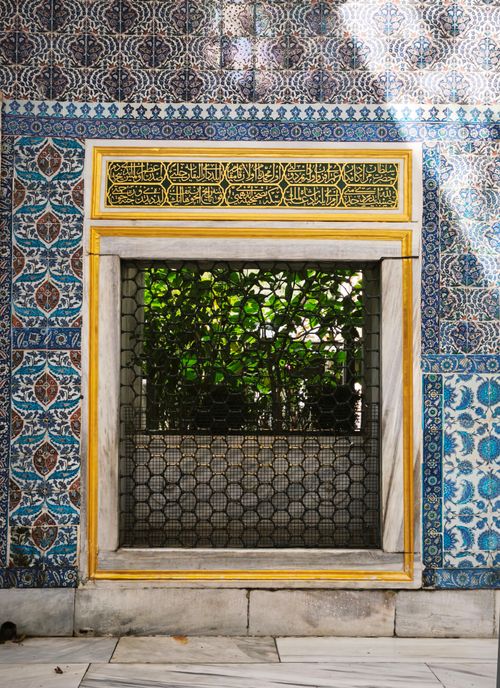 Free Beautiful ornate Islamic tile window revealing lush green foliage outside. Stock Photo