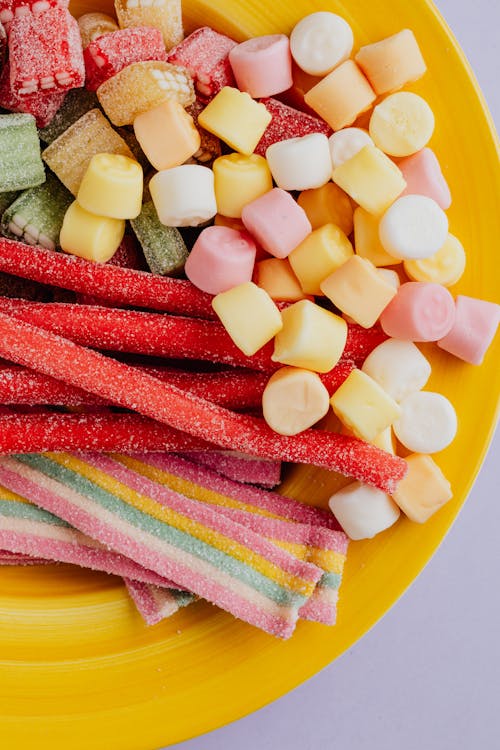 From above of set of natural multicolored marmalade candies in yellow ceramic plate on gray background