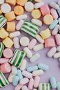 From above of various natural multicolored marshmallow and marmalade candies of different shapes on light purple background