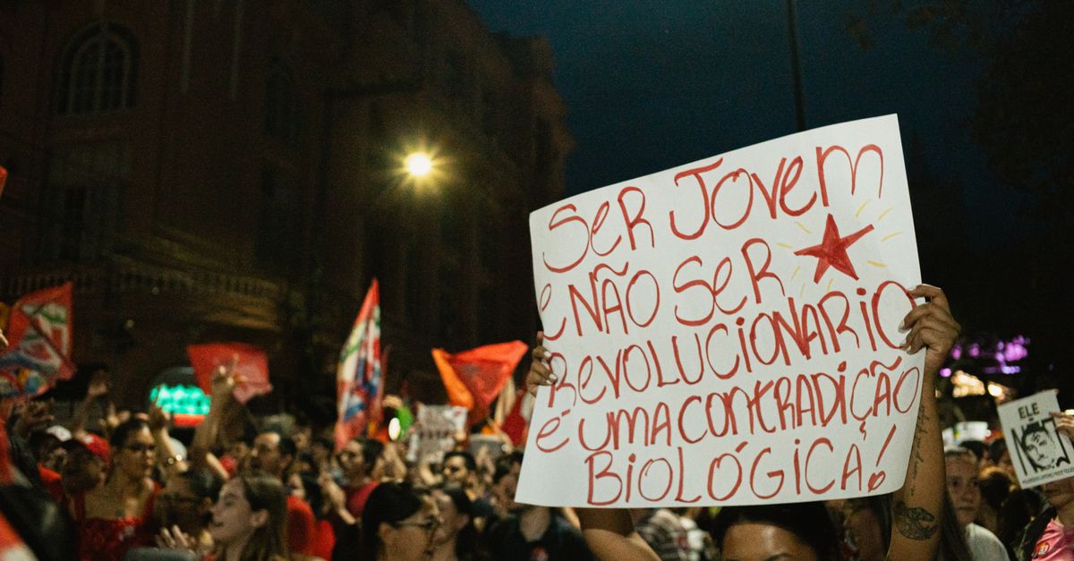 Crowd of young adults at a vibrant night protest holding red and white signs.