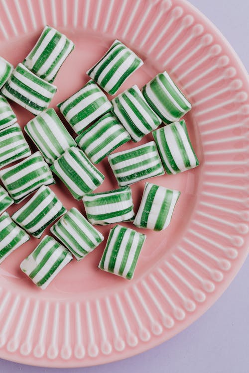 Top view of green and white candies with stripes placed on pink plate on purple background