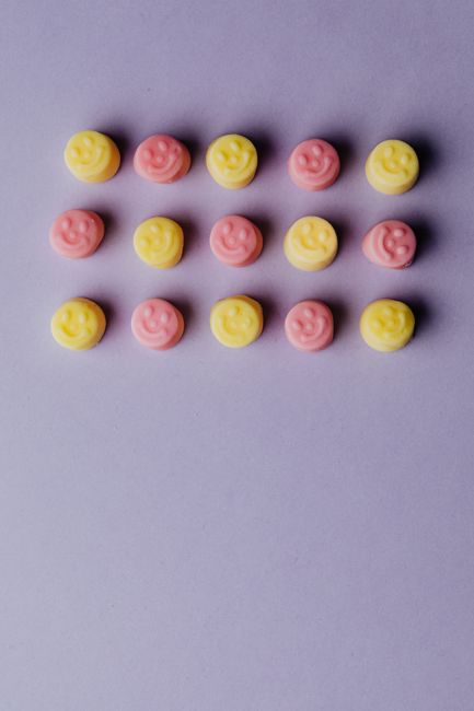 Arrangement of colorful smiley face gummies on a pastel purple background.