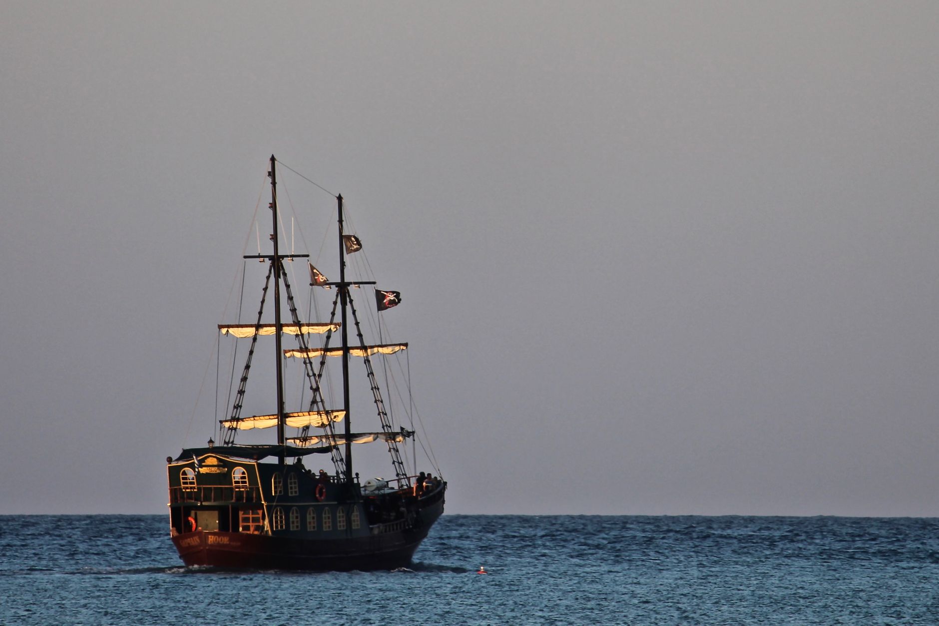 A vintage tall ship sails across the calm ocean at sunset, creating a picturesque maritime scene.