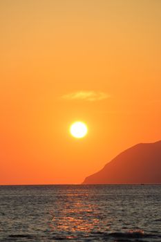 Beautiful sunset over the ocean with a vibrant orange sky and distant cliff silhouette.