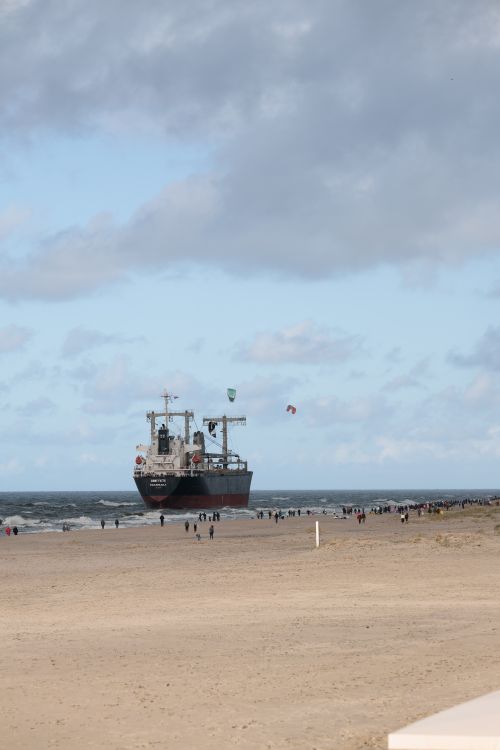 Free Cargo ship docked near a sandy beach in Kaliningrad Oblast, Russia with people strolling around and kites flying. Stock Photo