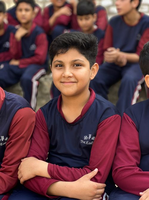 Free A smiling child in school uniform, seated outdoors in Khyber Pakhtunkhwa, Pakistan. Stock Photo
