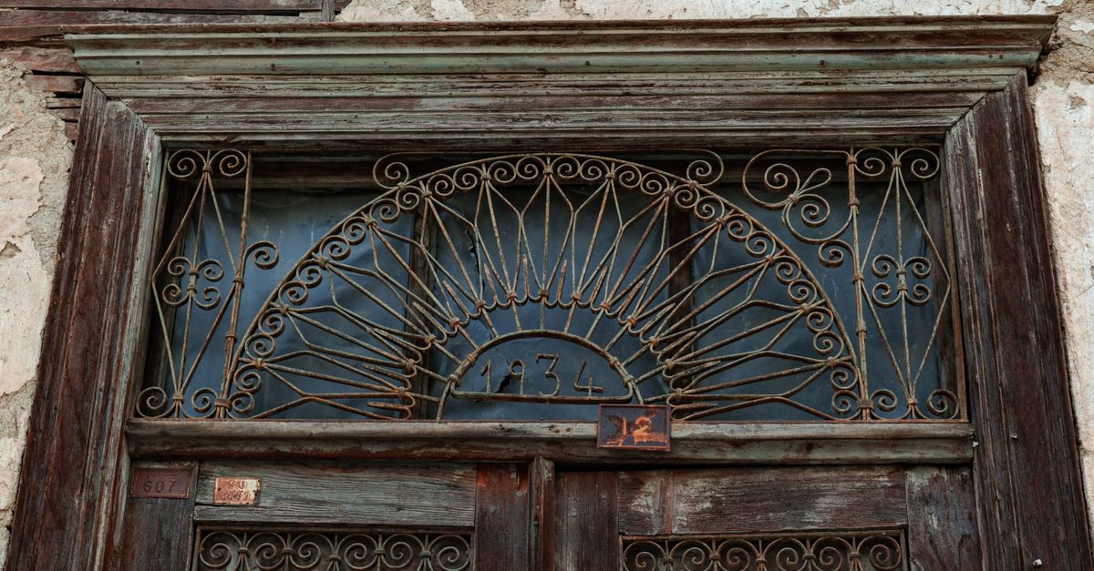Rustic wooden door with ornate iron grillwork and the year 1934 inscribed above. Weathered and vintage charm.