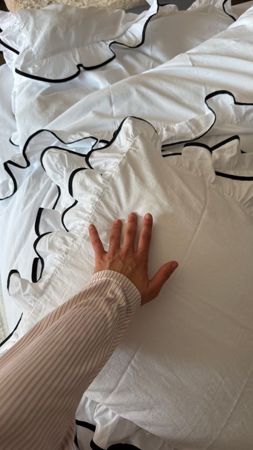 Free A hand gently rests on a ruffled white pillow atop an intricately made bed, suggesting comfort and elegance. Stock Photo