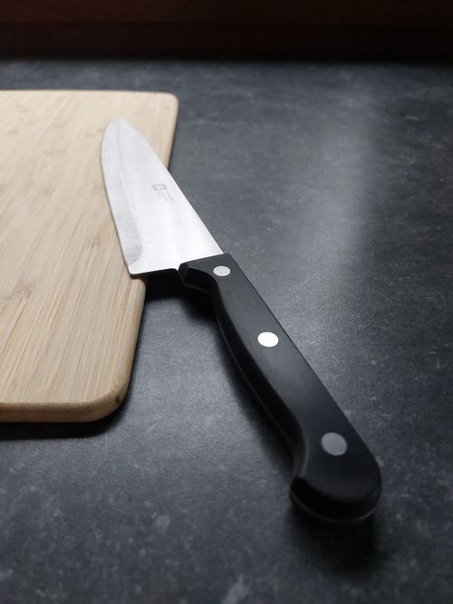 Free A sharp kitchen knife resting on a wooden cutting board on a dark countertop. Stock Photo