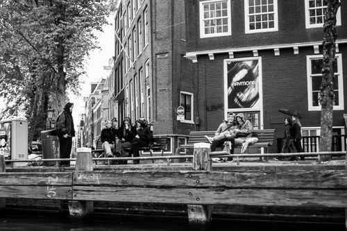 Free Black and white street scene with people sitting by a canal in Amsterdam, Netherlands. Stock Photo