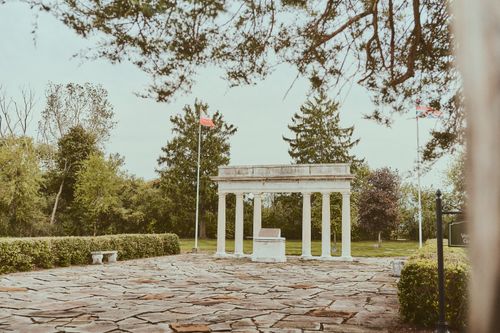Free A serene park with historic stone columns surrounded by lush green trees and flags. Stock Photo