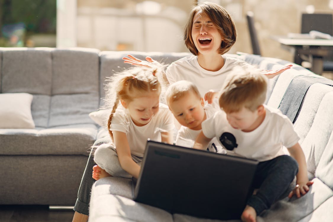 Free Stressed woman asking for help while sitting with small children playing on laptop together on sofa in living room Stock Photo