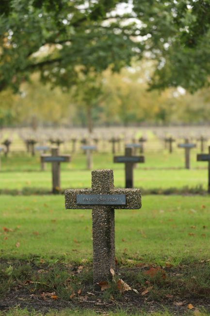 Fotomural Lápida de un soldado alemán en un tranquilo cementerio belga rodeado de frondosos árboles.