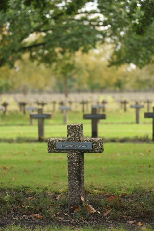 Free German soldier gravestone in a peaceful Belgium cemetery surrounded by lush trees. Stock Photo
