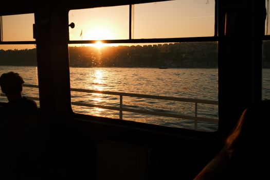 Silhouette of a person on a ferry with a stunning sunset over calm waters.