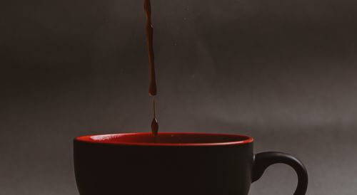 Free Elegant pour of coffee into a stylish black mug with red interior. Stock Photo