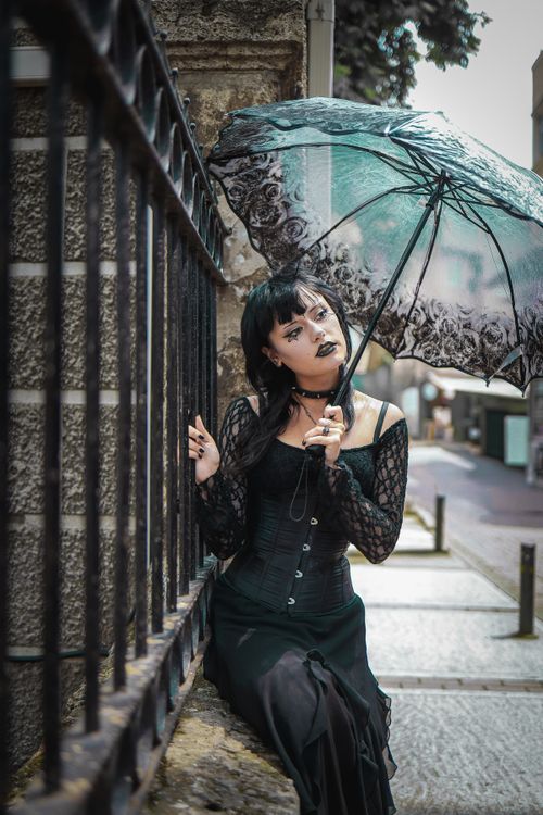 Free A gothic dressed woman stands under a decorative umbrella in a cityscape. Stock Photo