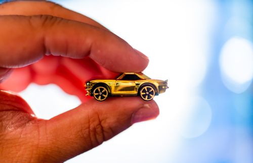 Free Detailed view of fingers gently holding a small gold toy car with blurred background. Stock Photo