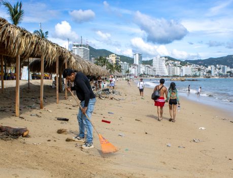 Volunteers cleaning a beach in Acapulco, Mexico with city skyline in the background.