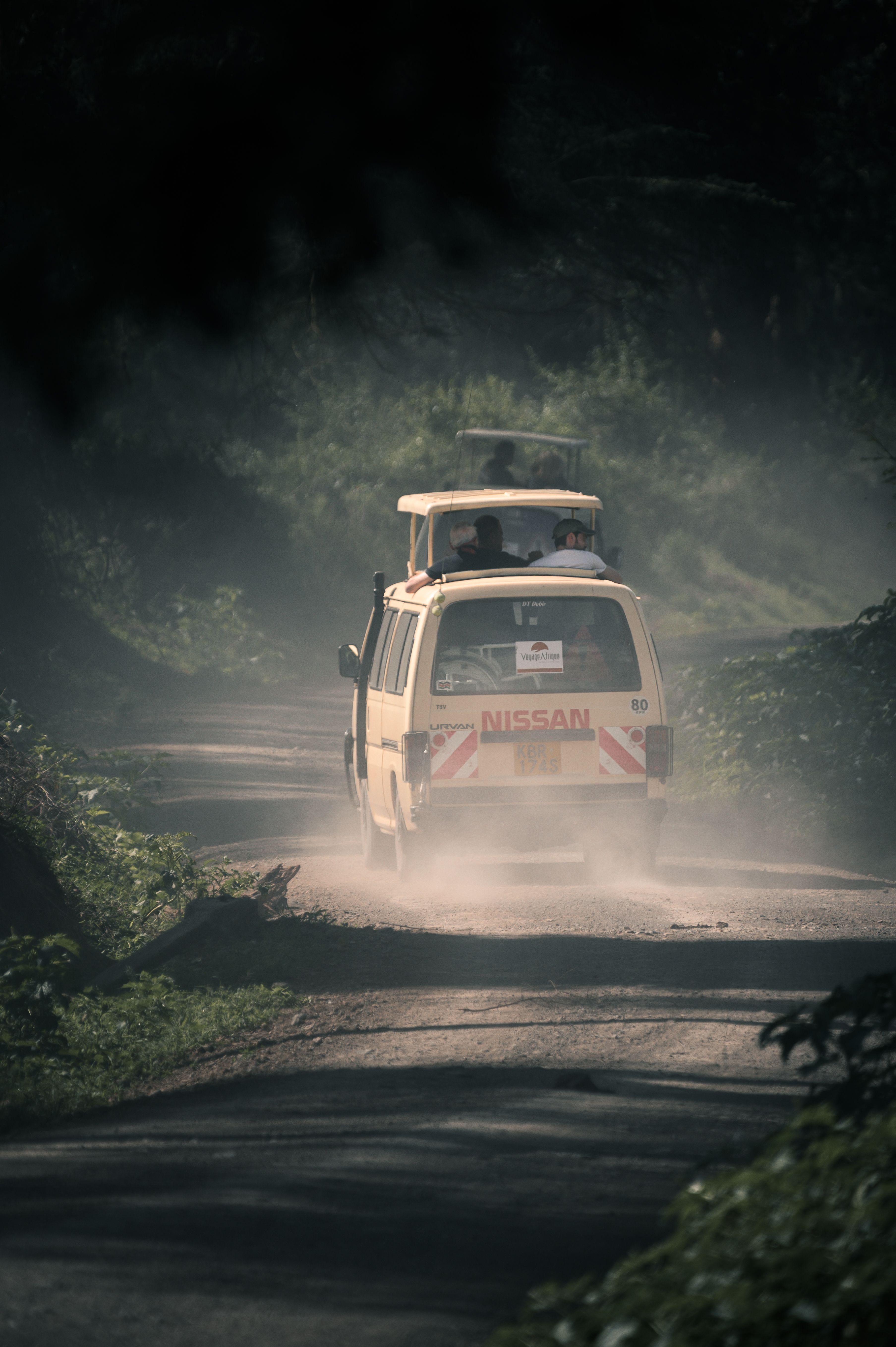 A safari van travels along a misty, unpaved road in Kenya's lush wilderness.