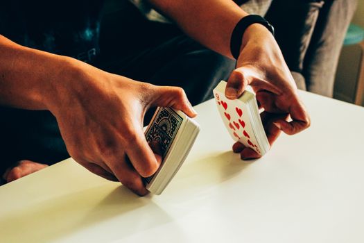 A person skillfully shuffles a deck of poker playing cards on a table indoors.