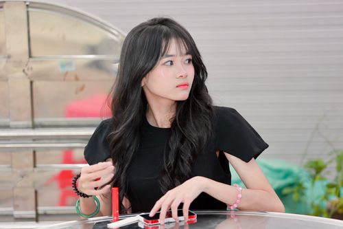 Free Young woman with long black hair sitting at a table, looking pensively to the side. Stock Photo