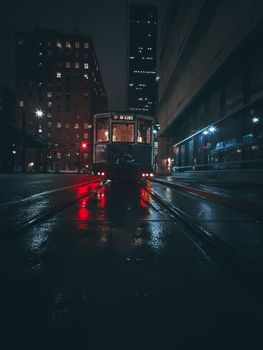夜晚，一辆电车驶过城市街道，潮湿的人行道和明亮的建筑物上倒映着它的身影