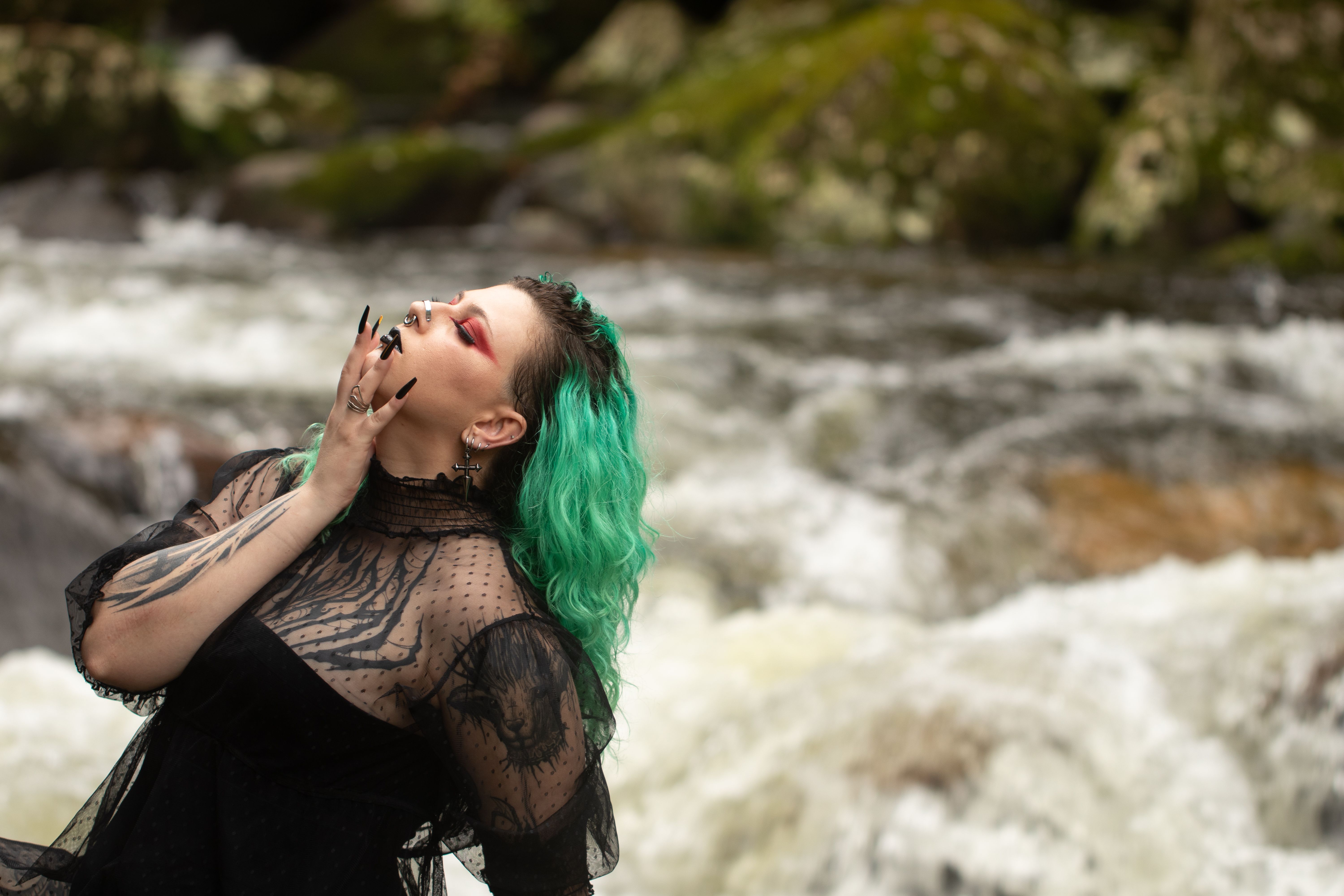 A striking portrait of a woman with green hair and tattoos, set by a rushing river.