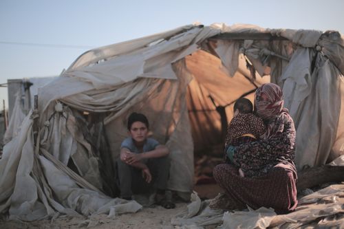 Free A mother holding her baby outside a torn tent next to a young child. Stock Photo