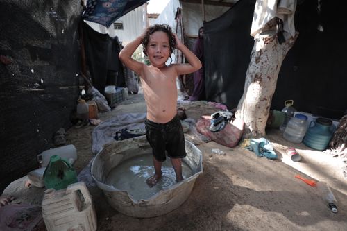 Free Smiling child bathes in a basin, surrounded by household items in a rustic setting. Stock Photo