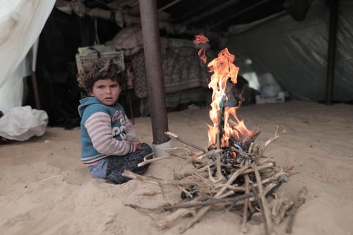 Free A child sits by a campfire inside a tent, creating a warm and rustic scene. Stock Photo