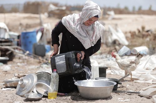 Free A woman in traditional attire pouring water from a black container into a basin outdoors. Stock Photo