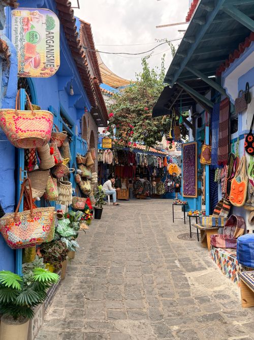Free Charming alley of colorful shops in Chefchaouen, Morocco, showcasing local crafts and vibrant decor. Stock Photo