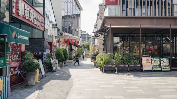 Street view of Asian market with shops, signage, and pedestrians on a sunny day.