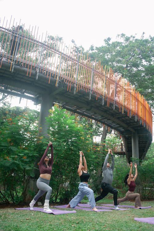 Free Four adults practicing yoga under a vibrant outdoor bridge amidst lush greenery. Stock Photo