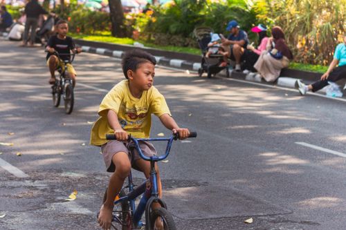 Free Kids cycling along a park road surrounded by families enjoying a sunny day outdoors. Stock Photo
