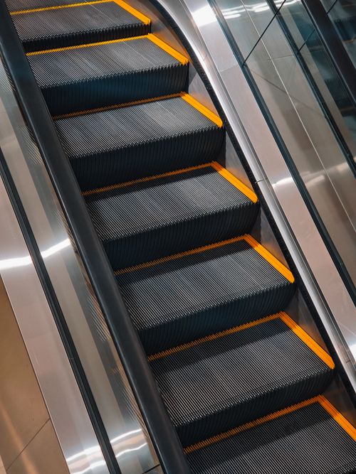 Free Close-up of a modern escalator's steps with distinctive yellow edges in an indoor setting. Stock Photo