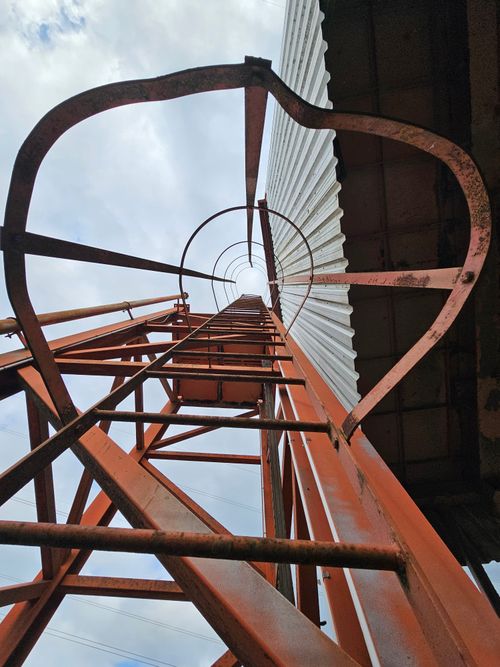 Free Looking up a rusted metal ladder against a cloudy sky, offering an abstract perspective. Stock Photo
