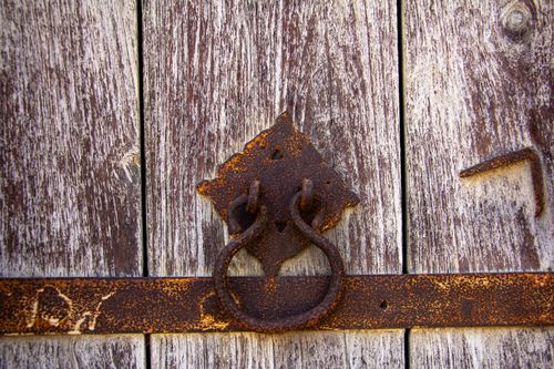 Free Close-up of a rustic, weathered wooden door featuring a rusty iron door handle. Stock Photo