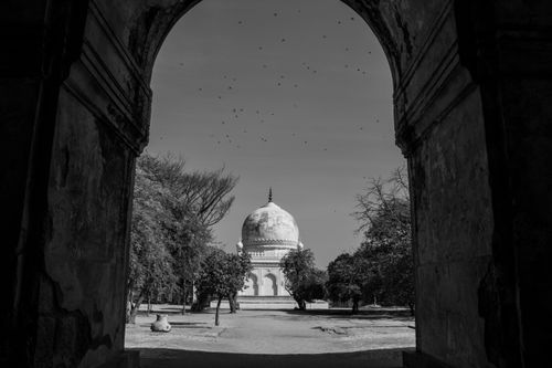 Free Black and white photo of a historic tomb seen through an arched doorway. Stock Photo