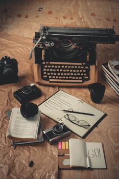 Nostalgic scene with a vintage typewriter, cameras, books, and writing tools on a wooden surface.
