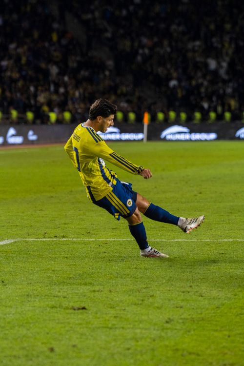 Free A soccer player in a yellow jersey kicking the ball during a night match in Baku, Azerbaijan. Stock Photo